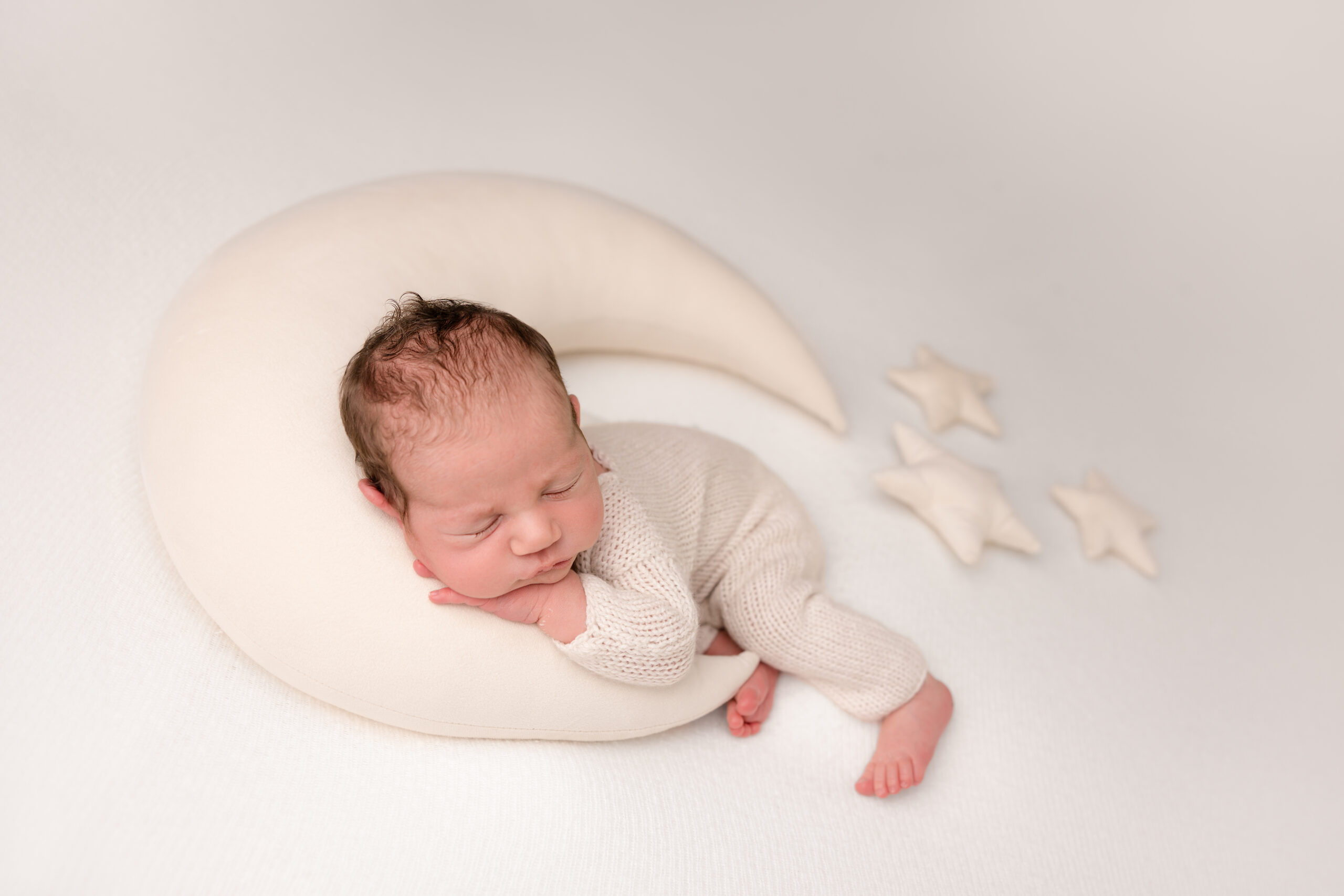 newborn photo session in London baby boy is sleeping on a white background on a moon prop